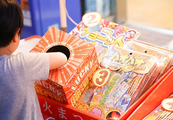 子どもが番号付きのくじ引き箱に手を入れている四の橋夏まつりの縁日屋台