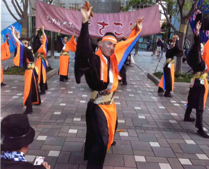 オレンジと黒の衣装を着たよさこいの踊り手が腕を上げて演舞する様子