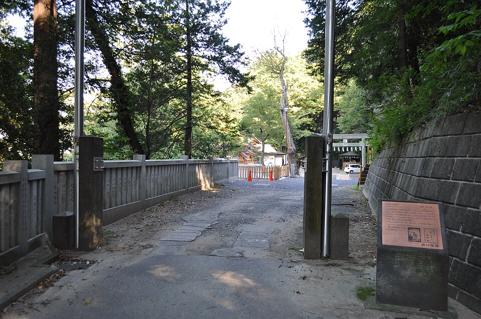穴澤天神社の参道入口。三沢川に架かる橋の先に鳥居と社殿が見え、右手に案内板が立っている