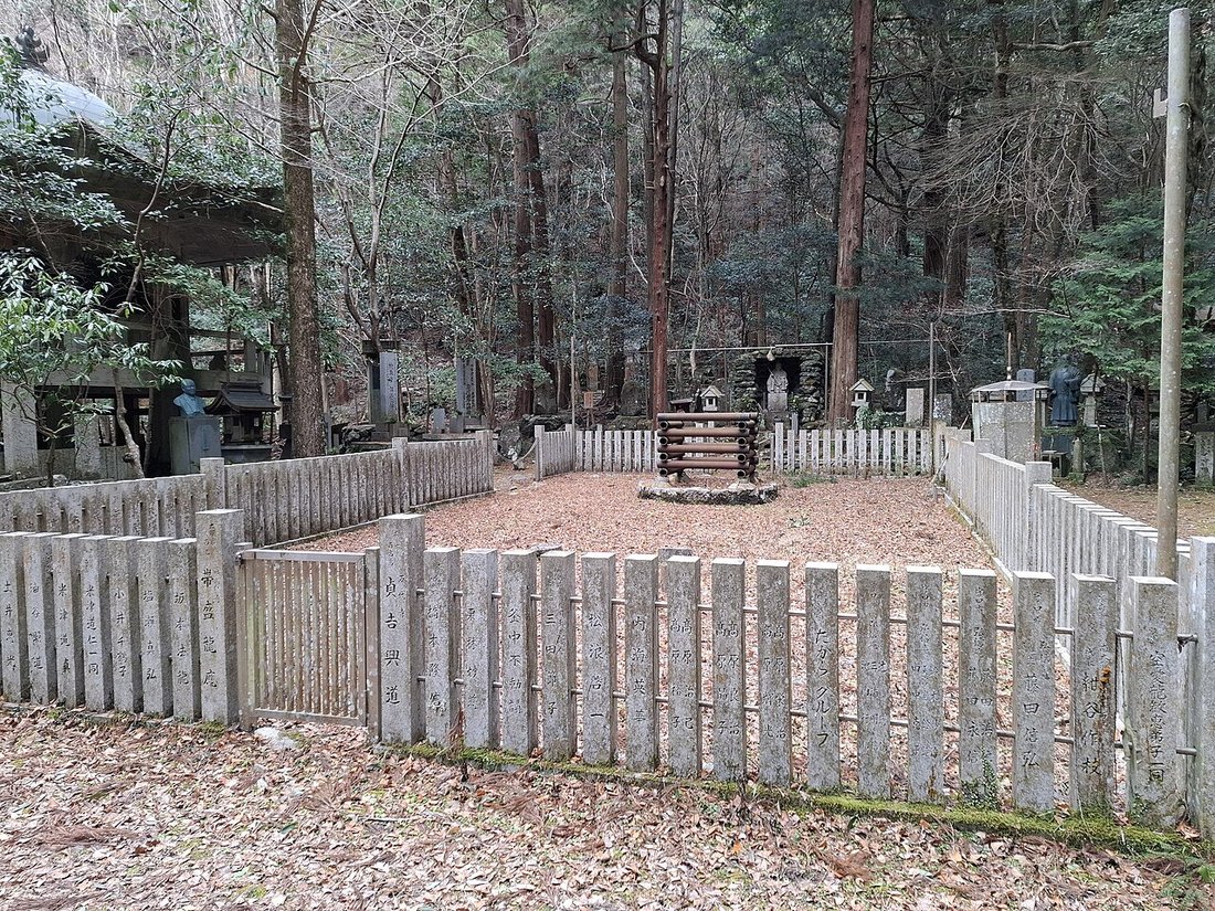犬鳴山七宝瀧寺の境内。玉垣に囲まれた広場の中央に、丸太を井桁に組んだ護摩壇が据えられ、周囲を杉木立が囲む