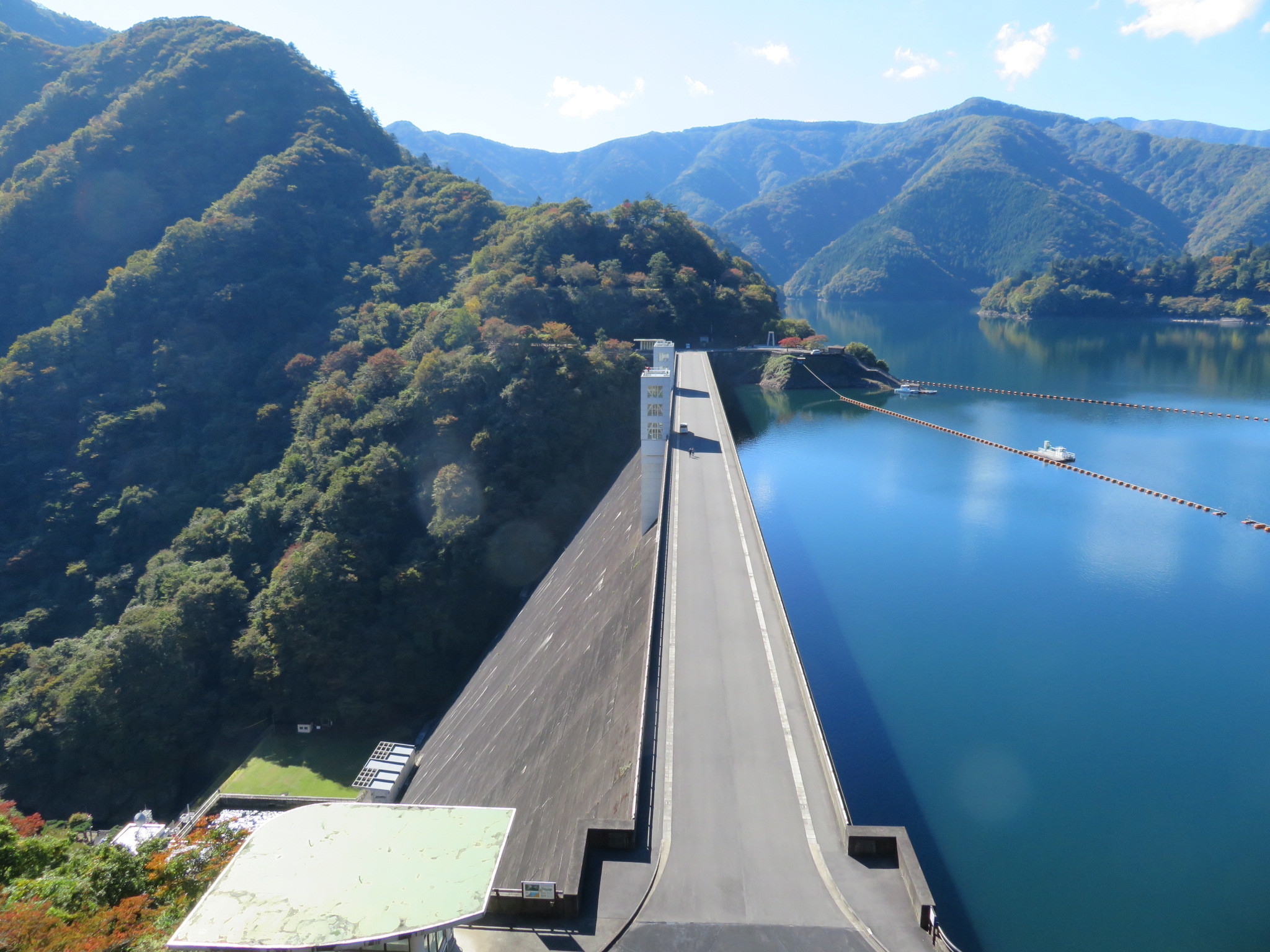 小河内ダムの堤頂道路と、その先に広がる奥多摩湖。両岸に山が迫っている