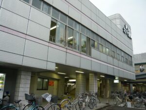 阪急千里線 北千里駅の東口。白いタイル張りの駅ビルに駅名看板が掲げられ、手前に自転車が並ぶ