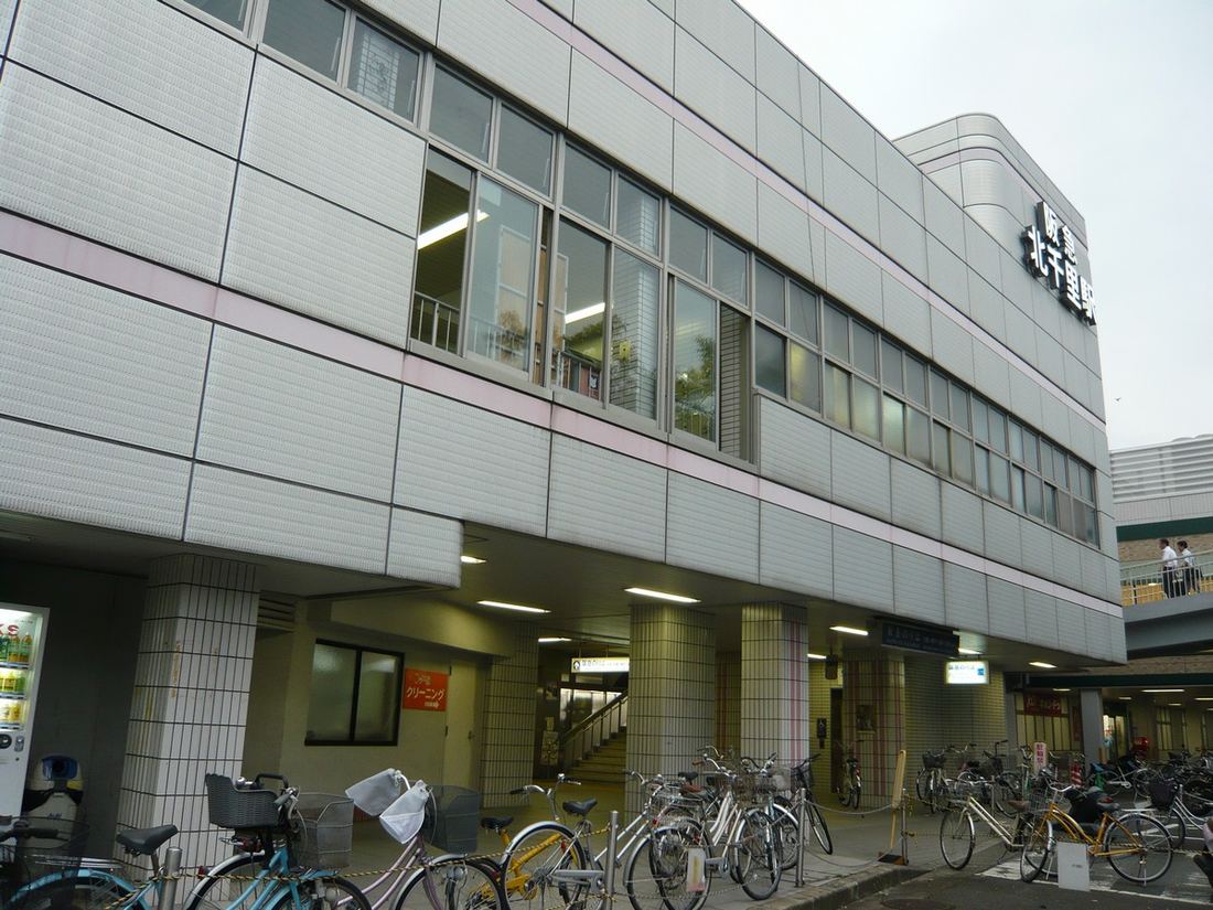 阪急千里線 北千里駅の東口。白いタイル張りの駅ビルに「阪急 北千里駅」の看板が掲げられ、手前に自転車が並んでいる
