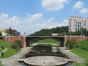 長池公園の姿池に架かる長池見附橋。赤レンガの橋台と鉄のアーチ、橋の下の水面と円形の石張り舞台