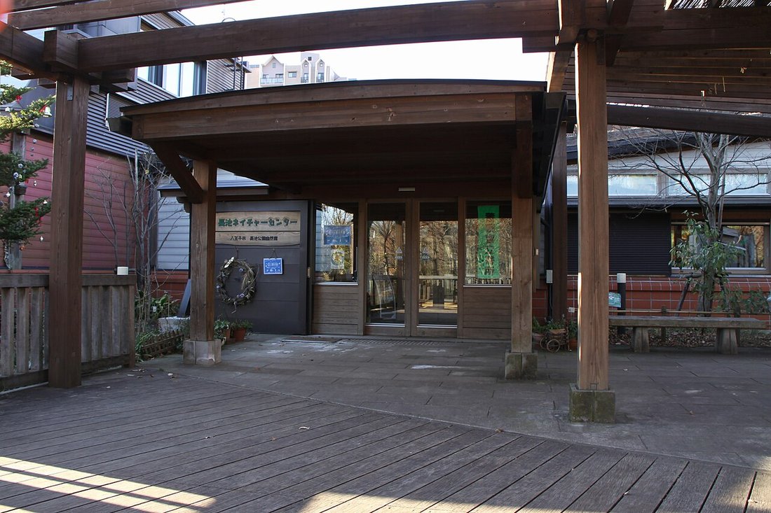 長池公園自然館の入口。木造の庇と柱、ガラスの自動ドア、「長池ネイチャーセンター 八王子市 長池公園自然館」の看板