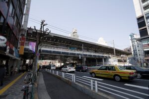中目黒駅の高架駅舎と山手通り。手前をタクシーが走り、歩道を人が歩いている
