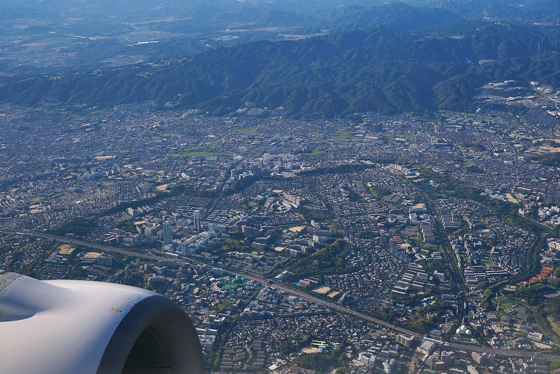 上空から見た千里ニュータウン一帯。丘陵地に中高層住宅と緑地が入り混じり、奥に山並みが連なる