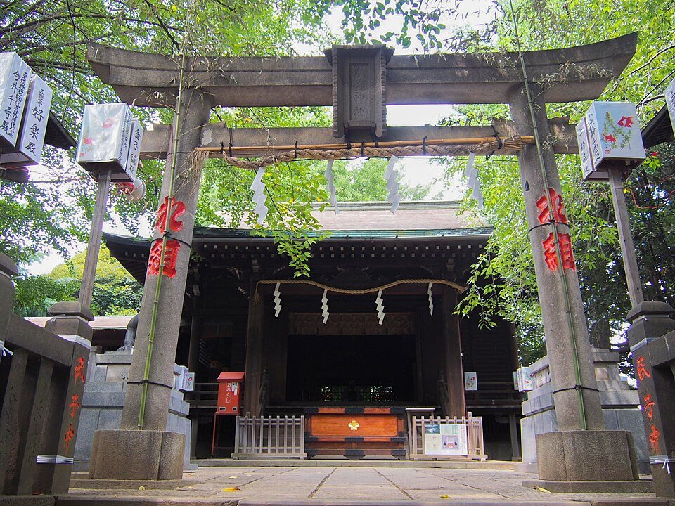 諏方神社の石鳥居と注連縄、その奥に建つ拝殿。左右の玉垣に奉納提灯が下がり、夏の緑が濃い境内
