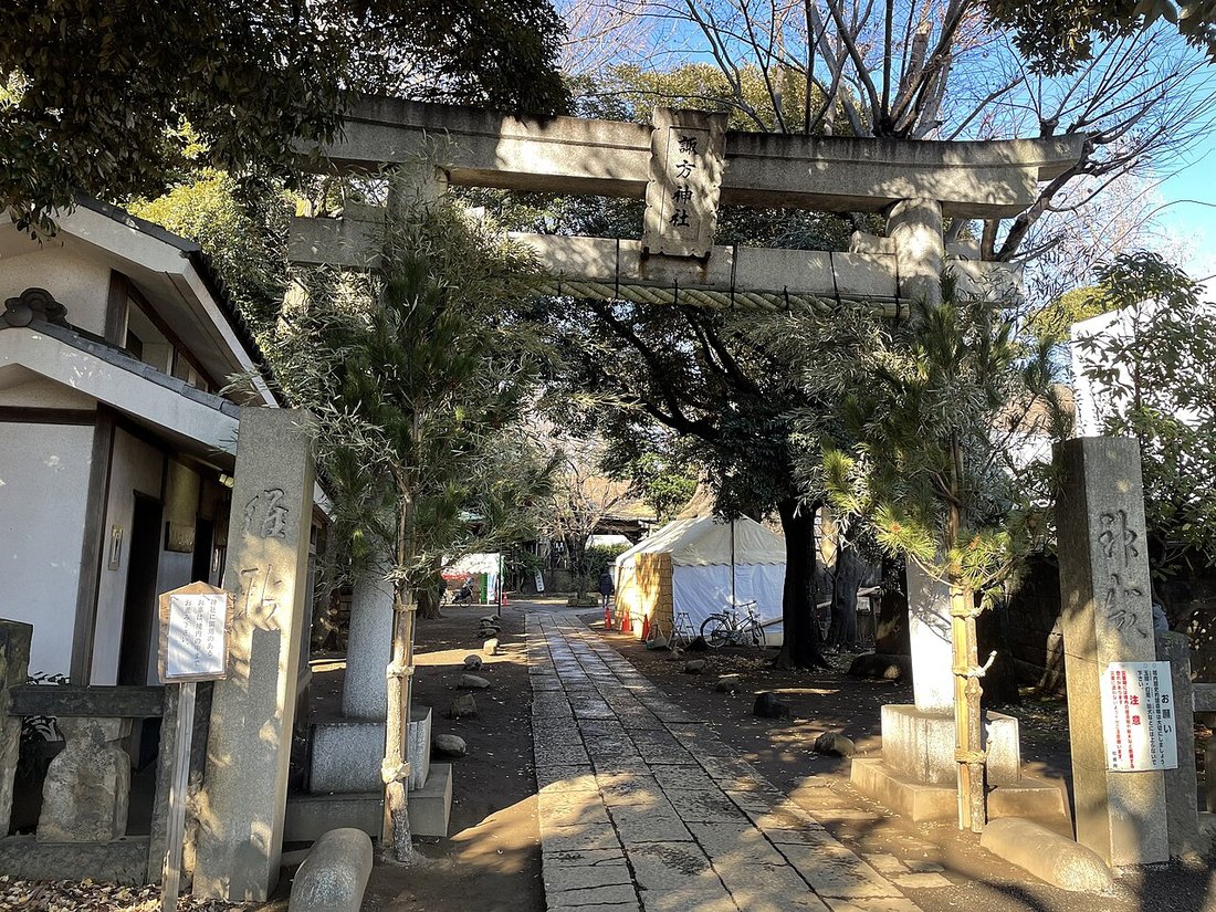 諏方神社の参道入口。「諏方神社」の額が掛かる石鳥居と、奥へまっすぐ延びる石畳の参道、右手にテント